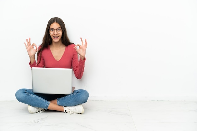 Młoda Francuzka siedzi na podłodze ze swoim laptopem i pokazuje palcami znak ok