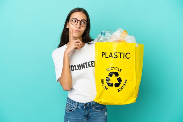 Młoda Francuzka trzymająca torbę pełną plastikowych butelek do recyklingu, mająca wątpliwości, patrząc w górę