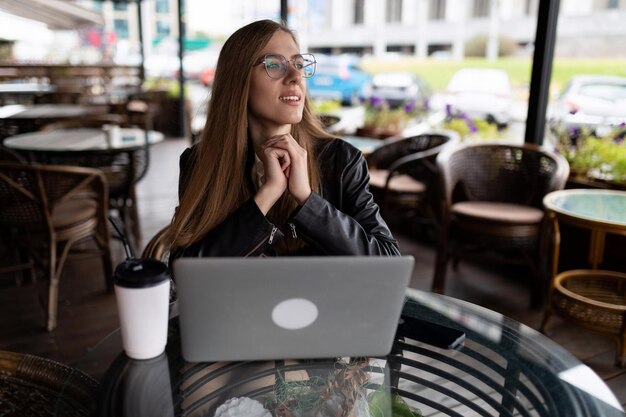 Młoda freelancerka pracująca na laptopie w miejskiej kawiarni