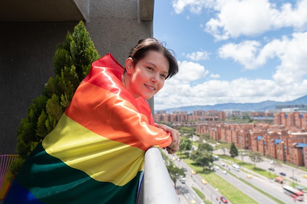 młoda gejowska kobieta patrząca ze swojego balkonu dumnie nosząca flagę LGBT w słoneczny dzień Wysoka jakość