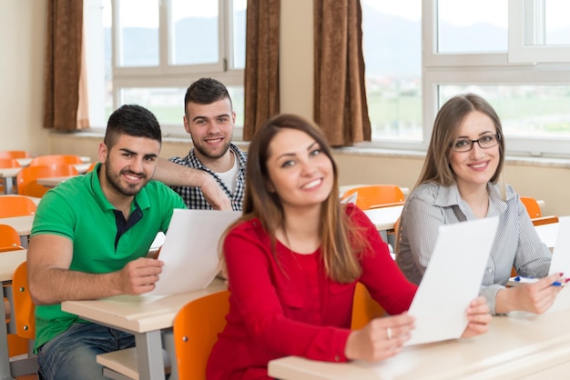 Młoda grupa atrakcyjnych nastoletnich uczniów w klasie w college'u, siedzących przy stole, uczących się lekcji