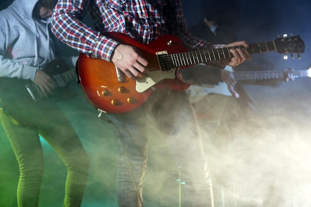 Młoda grupa gra na gitarze elektrycznej na oświetlonym mglistym tle
