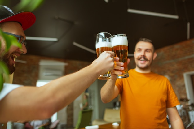 Młoda grupa przyjaciół pijąca piwo, bawiąca się, śmiejąca się i świętująca razem. Dwóch mężczyzn stuka się szklankami piwa. Oktoberfest, przyjaźń, wspólnota, koncepcja szczęścia.