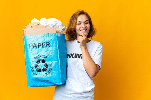 Młoda Gruzińska dziewczyna trzyma worek recyklingu pełnego papieru do recyklingu, patrząc z boku i uśmiechnięty