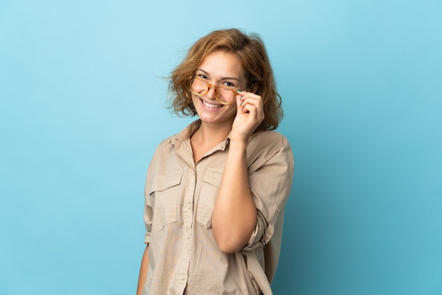 Młoda Gruzińska kobieta odizolowywająca na niebiesko w okularach i szczęśliwa