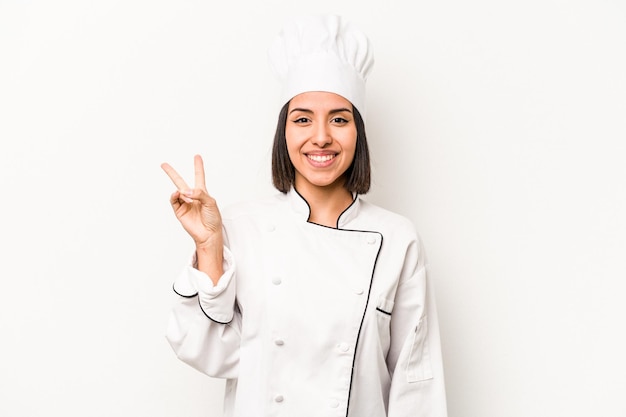 Młoda hiszpańska kobieta kucharz na białym tle radosna i beztroska pokazująca symbol pokoju palcami