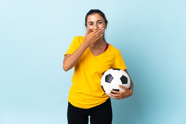 Młoda hiszpańska piłkarz kobieta na białym tle na niebieskiej ścianie szczęśliwa i uśmiechnięta obejmująca usta ręką