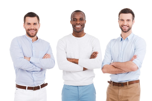 Młoda i odnosząca sukcesy. Trzech pewnych siebie młodych mężczyzn w eleganckim stroju na co dzień, trzymających ręce skrzyżowane i uśmiechniętych, stojąc na białym tle