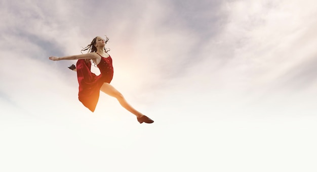 Zdjęcie młoda i piękna tancerka w czerwonej sukience skoki na niebie. różne środki przekazu