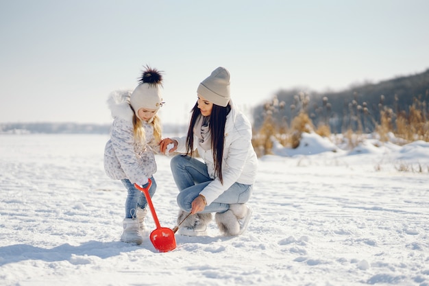 młoda i stylowa mama gra z jej małą córeczkę w parku śniegu zimą