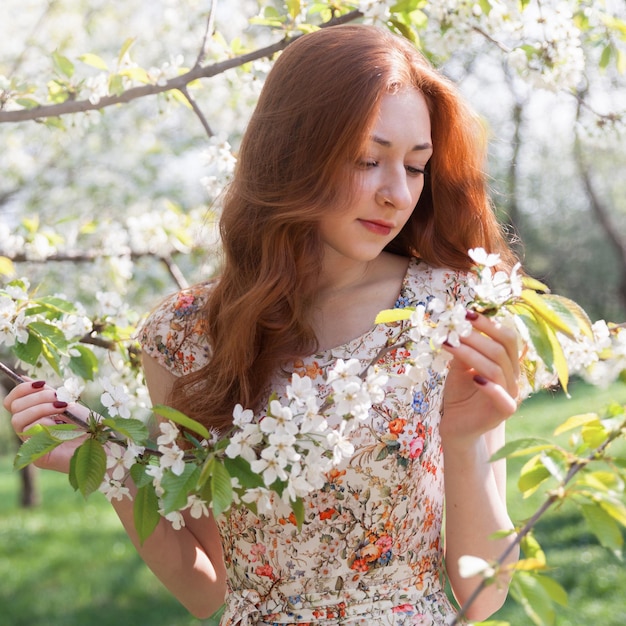 Młoda imbirowa włosiana kobieta w pobliżu białego delikatnego kwitnącego drzewa. baśniowy nastrój wiosny i lata. Piękna romantyczna pani uśmiechnięta panna młoda, ślub. Skopiuj tło.