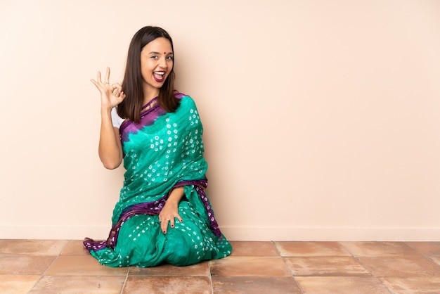 Młoda Indiańska kobieta siedzi na podłodze pokazano ok znak palcami