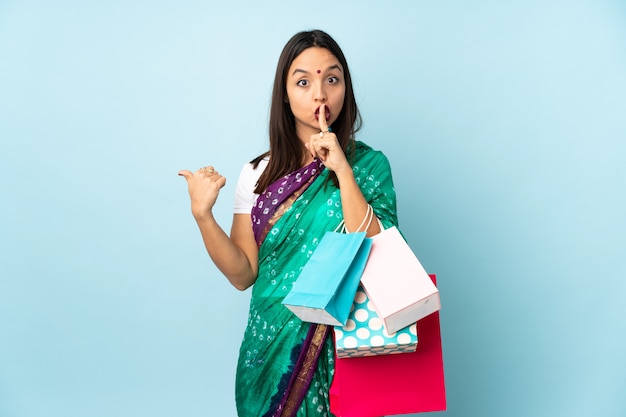 Młoda Indiańska kobieta wskazuje z boku i robi cisza gestowi z torba na zakupy