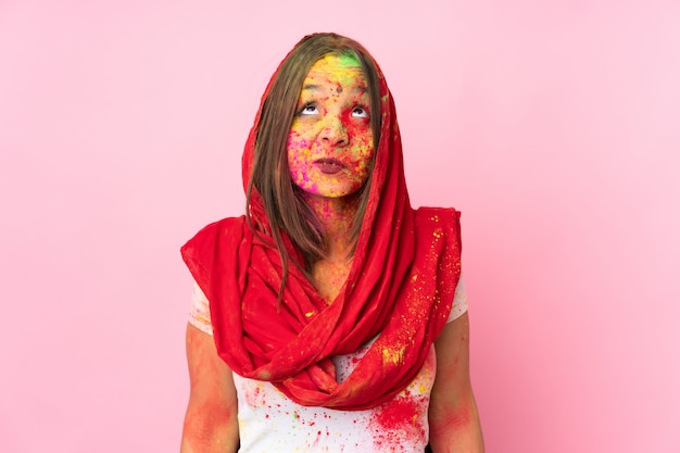 Młoda Indiańska kobieta z kolorowymi holi proszkami na jej twarzy na menchii ścianie i przyglądającym up