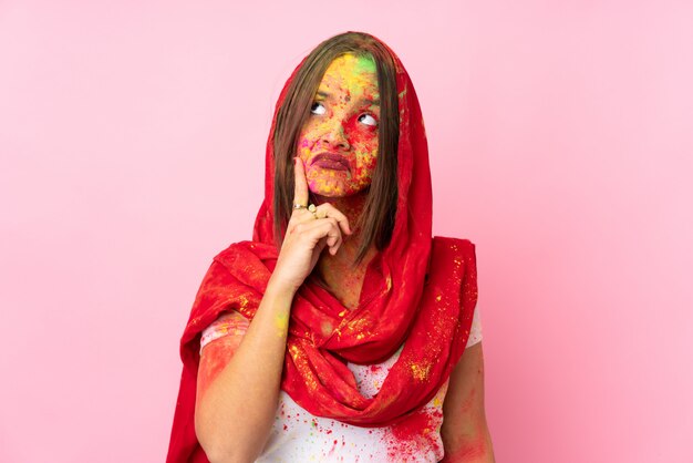 Młoda Indiańska kobieta z kolorowymi holi proszkami na jej twarzy odizolowywającej na menchii ścianie