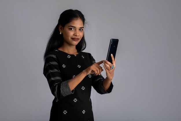 Młoda indyjska dziewczyna za pomocą telefonu komórkowego lub smartfona na szaro