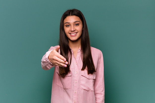 Młoda indyjska kobieta na białym tle na niebieskiej ścianie, rozciągając rękę w geście pozdrowienia.