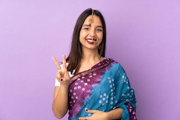 Młoda indyjska kobieta na białym tle uśmiechając się i pokazując znak zwycięstwa