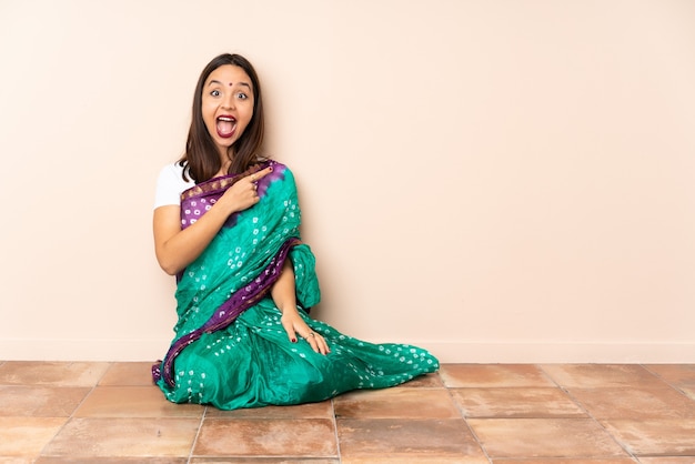Młoda indyjska kobieta siedzi na podłodze zaskoczony i wskazuje stronę