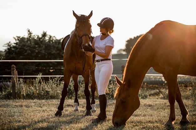 Młoda jeździec ubrana w biały sportowy strój i kask rozmawiający ze swoim koniem po treningu drugiego konia stoi obok niej Koncepcja miłości i zrozumienia ze zwierzętami