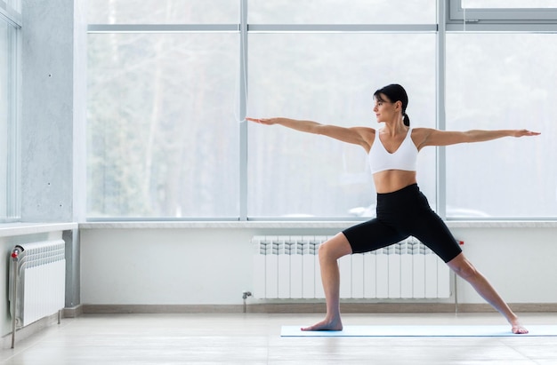 Młoda joginka ćwicząca jogę stojąca w pozie wojownika w dwóch ćwiczeniach Virabhadrasana II