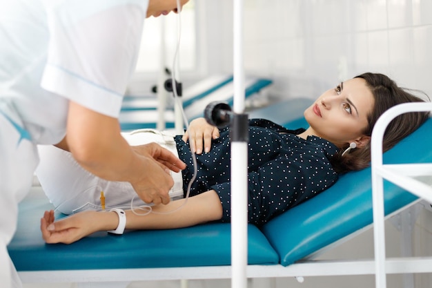 Młoda kaukaska brunetka kobieta na kanapie medycznej pod kroplówką medyczną Koncepcja procedury medycznej