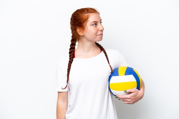 Młoda kaukaska czerwonawo kobieta gra w siatkówkę na białym tle patrząc w bok