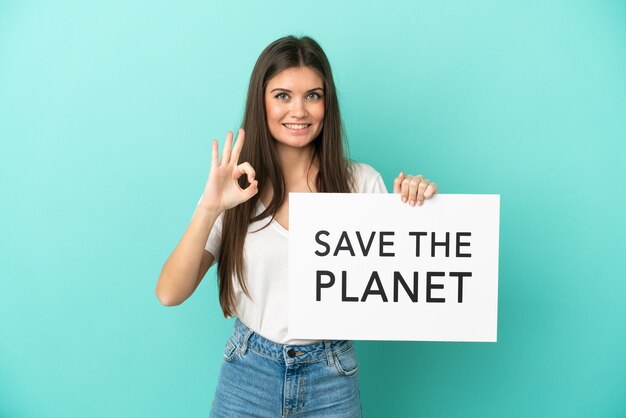 Młoda kaukaska kobieta na białym tle na niebieskim tle trzyma afisz z tekstem Save the Planet i świętuje zwycięstwo