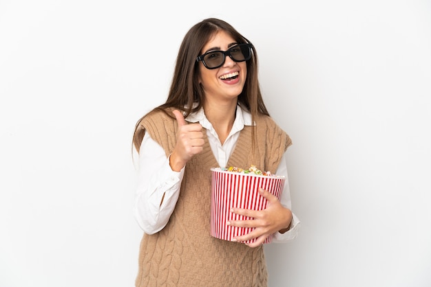 Młoda kaukaska kobieta na białym tle w okularach 3d i trzymająca duże wiadro popcornów, wskazując przód