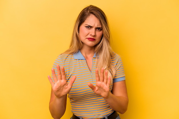 Młoda kaukaska kobieta na żółtym tle odrzuca kogoś pokazującego gest obrzydzenia