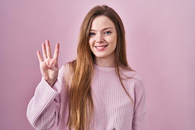 Młoda kaukaska kobieta stojąca na różowym tle, pokazująca i wskazująca palcami numer cztery, uśmiechając się pewna siebie i szczęśliwa.