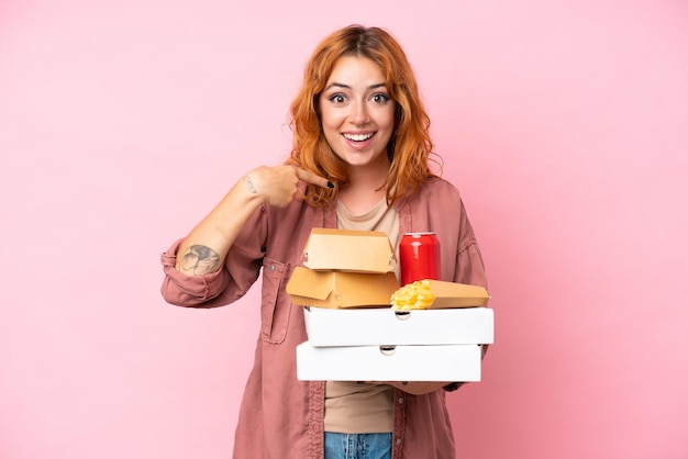 Zdjęcie młoda kaukaska kobieta trzyma fast food odizolowany na różowym tle z niespodzianką wyraz twarzy