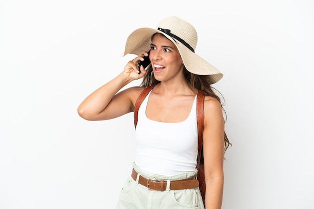 Młoda kaukaska kobieta ubrana w Pamelę w letnie wakacje na białym tle, prowadząca rozmowę z telefonem komórkowym z kimś