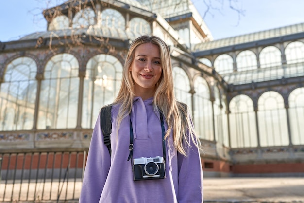 Młoda kaukaska kobieta uchwyciła radość z podróży swoim aparatem przed kryształowym pałacem w Madrycie