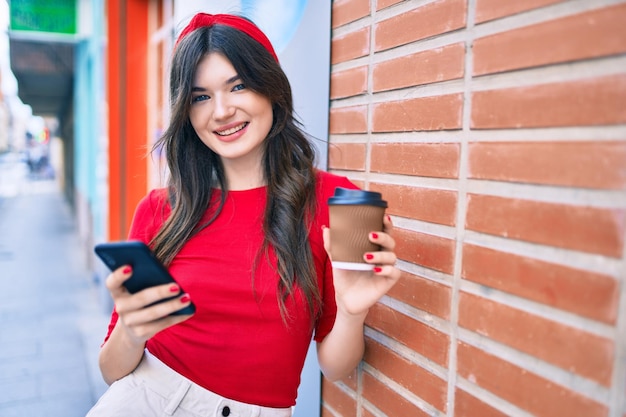 Młoda kaukaska kobieta używająca smartfona i pijąca kawę na wynos w mieście