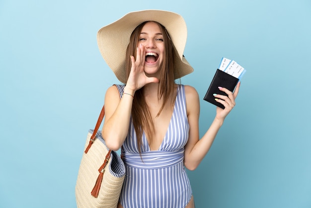 Młoda kaukaska kobieta w letnie wakacje trzymająca paszport na białym tle na niebieskim tle krzycząca z szeroko otwartymi ustami