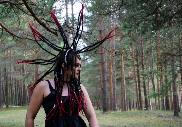Młoda kaukaska kobieta z czarnymi i czerwonymi punkowymi włosami pozuje w lesie