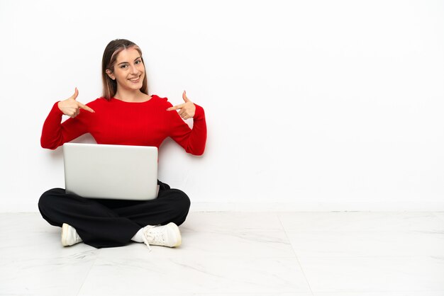 Młoda kaukaska kobieta z laptopem siedzi na podłodze dumna i zadowolona z siebie