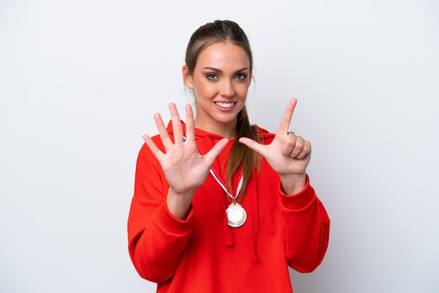 Młoda kaukaska kobieta z medalami na białym tle, licząc siedem palcami