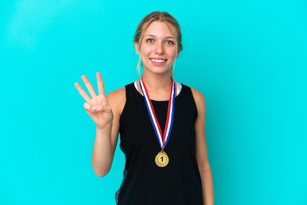 Młoda kaukaska kobieta z medalami na białym tle na niebieskim tle szczęśliwa i licząca trzy palcami