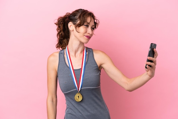 Młoda kaukaska kobieta z medalami na różowym tle robi selfie
