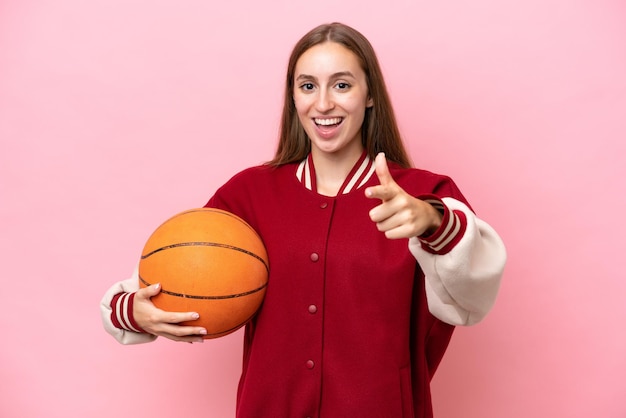 Młoda kaukaska koszykarz kobieta na białym tle na różowym tle zaskoczona i wskazująca przód