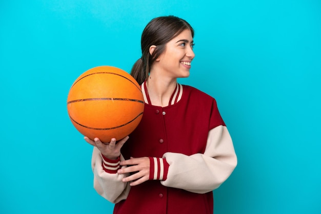 Młoda kaukaska koszykarz kobieta odizolowana na niebieskim tle patrząc z boku