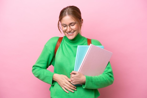 Młoda kaukaska studentka odizolowana na różowym tle uśmiecha się dużo