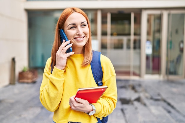 Młoda kaukaska studentka uśmiecha się pewnie rozmawiając na smartfonie na uniwersytecie