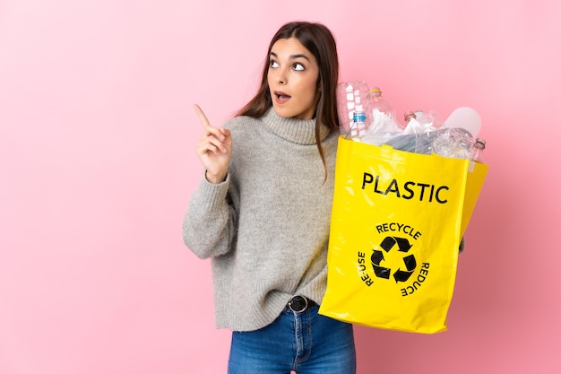 Młoda kaukaski kobieta trzyma torbę pełną plastikowych butelek do recyklingu na różowo