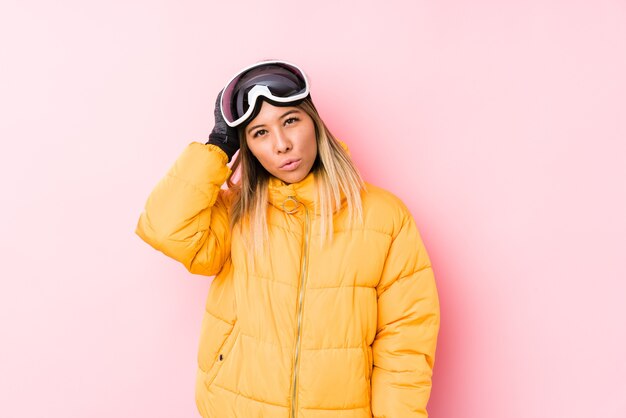 Młoda kaukaski kobieta ubrana w ubrania narciarskie w różowej ścianie zmęczona i bardzo senna, trzymając rękę na głowie.