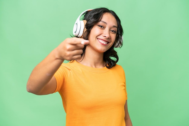 Młoda kaukazyjska argentyńska kobieta na odosobnionym tle słucha muzyki i wskazuje na przód