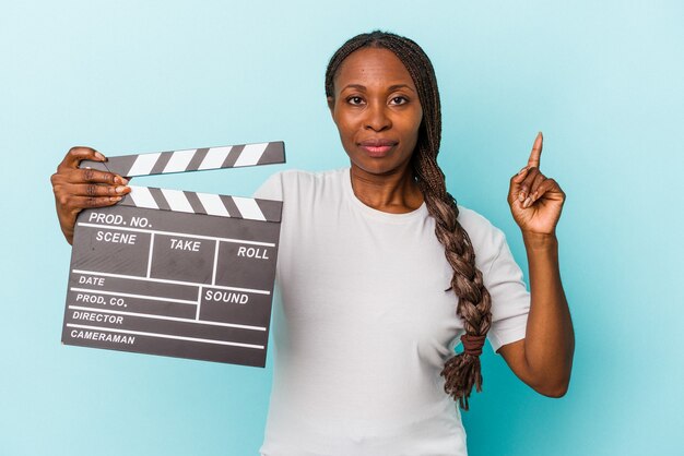 Młoda Kobieta African American Gospodarstwa Clapperboard Na Białym Tle Na Niebieskim Tle Pokazując Numer Jeden Palcem.