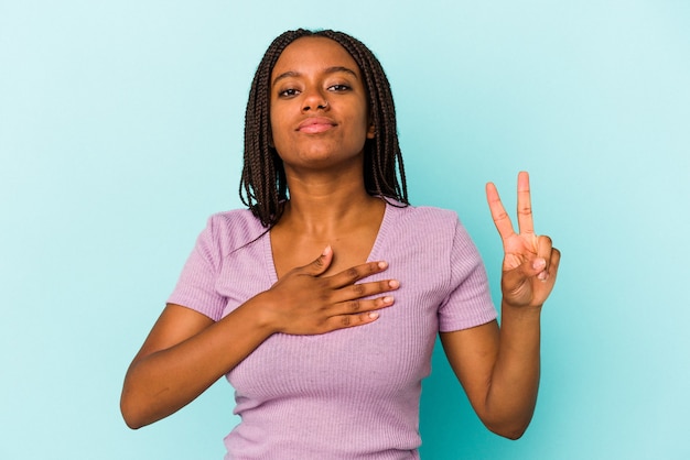 Młoda kobieta african american na białym tle na niebieskim tle, biorąc przysięgę, kładąc rękę na klatce piersiowej.